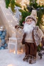 Santa Claus toy in brown clothes standing at white lantern. Fir tree branches and Christmas decorations on blurry background Royalty Free Stock Photo