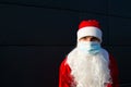 Santa Claus with white beard in red coat in a medical mask. Christmas in the coronavirus pandemic, seasonal diseases, SARS and pne