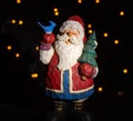 Santa clause figurine with blue bird on hand and a pine tree in the other hand. light points in the black background Royalty Free Stock Photo