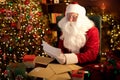 Santa Clause is prepares gifts for children for Xmas at his desk at home while reading wish lists Royalty Free Stock Photo