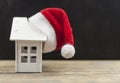 Santa hat with miniature house model over blank chalkboard Royalty Free Stock Photo