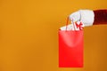 Santa holding paper bag with gift boxes on orange background, closeup. Space for text Royalty Free Stock Photo