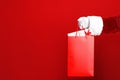 Santa holding paper bag with gift boxes on red background, closeup. Space for text Royalty Free Stock Photo
