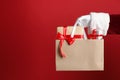 Santa holding paper bag with gift boxes on red background, closeup. Space for text Royalty Free Stock Photo