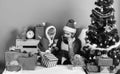 Santa and little assistant among gift boxes near fir tree. Royalty Free Stock Photo