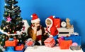 Santa and little assistant among gift boxes near fir tree. Royalty Free Stock Photo