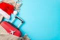 Overhead composition featuring a red suitcase, small plane model, Santa\'s outfit, and wintry details against blue background Royalty Free Stock Photo