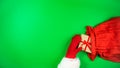 Santa`s hand in a red mitten puts gift boxes wrapped in craft paper and tied with red ribbon into a red bag. Green background Royalty Free Stock Photo