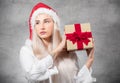 Santa woman with christmas gift on gray background. Thinkful young girl wearing red santa hat and holding present box