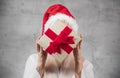 Santa woman holding christmas gifts and covering his face, isolated on gray background. Happy young girl wearing red santa hat and Royalty Free Stock Photo