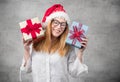 Santa woman holding christmas gifts isolated on gray background. Happy young girl wearing red santa hat and holding present box Royalty Free Stock Photo