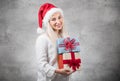 Santa woman holding christmas gifts isolated on gray background. Happy young girl wearing red santa hat and holding present box Royalty Free Stock Photo