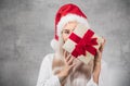 Santa woman holding christmas gifts isolated on gray background. Happy young girl wearing red santa hat and holding present box Royalty Free Stock Photo