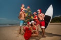 Santas` group wearing red bikini with Santa Claus, having fun on the beach, decorating the christmas tree with flip flops and Royalty Free Stock Photo