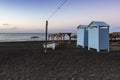 Santorini, black pebble beach of Perivolos, Perisa at sunrise. Two blue houses for changing. White-blue fishing boat and sunbeds Royalty Free Stock Photo