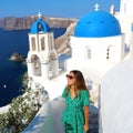 Santorini fashion woman visiting Oia, famous white village with blue domes in Greece. Girl in green dress and sunglasses Royalty Free Stock Photo