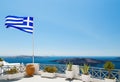 Santorini with flag on white balcony of hotel with flowers and pots of Greece, Fira capital town Royalty Free Stock Photo