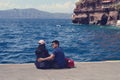 A young Chinese couple in love is sitting in the old port of the Greek city of Fira on the island of Santorini.