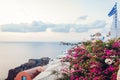 Santorini island Oia landscape. Traditional white houses and greek flag with sea and flowers view. Travel to Greece Royalty Free Stock Photo