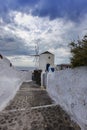 Santorini - Oia, Windmill, a stone path with a high white wall leading to a windmill. Beautiful sky with dramatic clouds Royalty Free Stock Photo