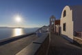 Santorini - picturesque white houses with a white bell tower built at the foot of a cliff falling into the sea. Beautiful sunset