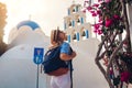 Santorini tourist with backpack walks by church with blue dome and blooming bougainvillea flowers in Akrotiri