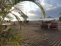 Sanur Beach view in the morning with restaurant table on white sand texture and palm leaves tree as foreground. Bali, Indonesia Royalty Free Stock Photo