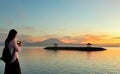 Sanur, Indonesia - April 1, 2019: A young lady standing capturing the sunrise & Mount Agung view early morning at Sanur Beach, Royalty Free Stock Photo