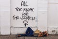 Homeless man sleeping on the ground with feminist writing on the wall