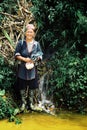 woman from the black hmong tribe standing next to a yellow colored stream and a small waterfall