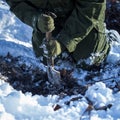 Sapper kneeling on the ground covered with snow is digging