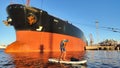 A sapsurfer swims in front of a huge tanker in the port of St. Petersburg.