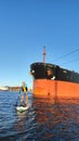 A sapsurfer swims in front of a huge tanker in the port of St. Petersburg.