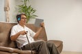 Sarcopenia older man is using digital tablet and headphone on sofa for relax at nursing home