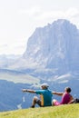 Hikers rest on the lawn admiring the Sassolungo mountain which is part of the Dolomites, Euro