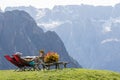 Hikers are resting on a deck chair admiring the Sassolungo mountain that is part of the Dolom