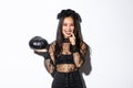 Sassy attractive asian woman in witch costume looking cunning and smiling, holding pumpking, going trick or treating on