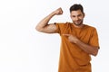 Sassy confident smiling macho man with big muscles, proudly pointing his hand as showing biceps on arm, pointing at hand Royalty Free Stock Photo