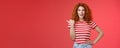 Sassy good-looking emotive happy smiling redhead european female curly hairstyle pointing thumb left grin assertive Royalty Free Stock Photo