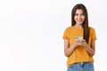 Sassy, happy good-looking woman in yellow t-shirt, holding smartphone look camera pleased and cheerful, shopping online