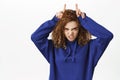 Sassy teen curly girl, shows horns, fingers on head gesture, bull sign, looks stubborn, stands over white background