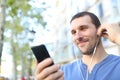 Satisfied adult man listening to music with earbuds in the street