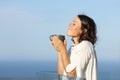 Satisfied adult woman smelling coffee in a balcony