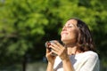 Satisfied adult woman smelling coffee cup in a park