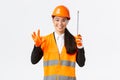 Satisfied asian female construction engineer, architect or inspector at enterprise showing okay gesture and tape measure