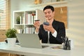 Satisfied asian male worker holding credit card and using smartphone for making orders via iInternet or online payment Royalty Free Stock Photo