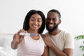 Satisfied attractive millennial black woman and guy show positive pregnancy test at camera in bedroom interior