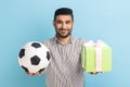 Satisfied businessman standing looking smiling at camera, holding out soccer ball and present box. Royalty Free Stock Photo