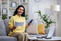 Satisfied businesswoman working from home, sitting on sofa in front of laptop, holding phone and documents, smiling and Royalty Free Stock Photo