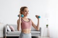 Satisfied caucasian cute millennial blonde woman lifts up dumbbells at home, free space